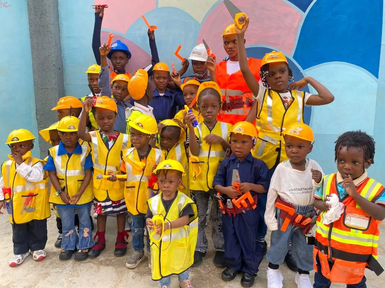 Young pupils in yellow hard hats and safety vests holding toy tools